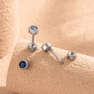 Silver geometric cartilage stud earring with round blue zircon stone on beige background