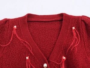 Dettaglio del cardigan in maglia rossa con bordi in piuma e bottoni di perla