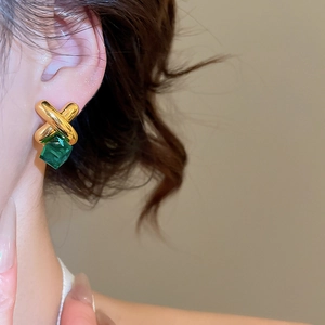 Detail of gold geometric cross earrings featuring a rectangular green faceted gemstone
