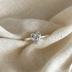 Minimalist 925 sterling silver ring with heart-shaped zircon on beige fabric background