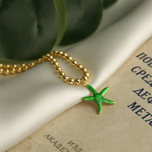 Detailed macro view of a gold-plated beaded chain with a green starfish enamel pendant
