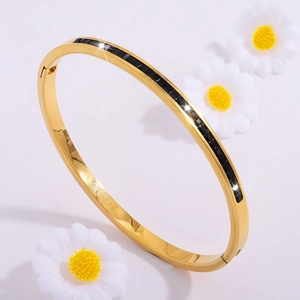 Elegante brazalete de acero de titanio dorado con circonitas negras en un fondo blanco