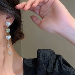 Close-up of elegant long heart pearl drop earrings worn by a model in soft light