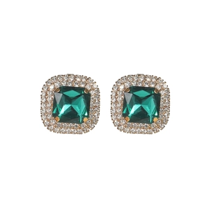 Macro shot of emerald cut green gemstone earrings with white zircon halo in gold
