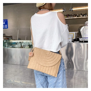 Detail of handwoven straw crossbody bag featuring a concentric flap and plush pom pom charm