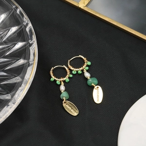 Detail view of handmade gold drop earrings with green beads and white pearls on black background