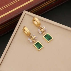 Golden hoop earrings with emerald square pendant and crystal bow on a leather jewelry box