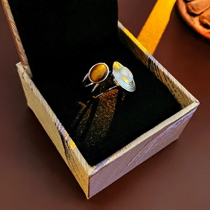 Detailed view of silver open ring with brown cat's eye and opal stones in a gift box