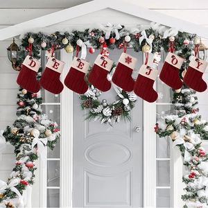 Set of red knitted Christmas stockings with letters hanging on a decorated white porch