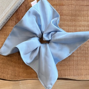 Detailed view of light blue silk scrunchie on a rustic wooden texture surface