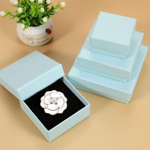 Macro view of light blue jewelry boxes with camellia brooch and pearl detail in soft light