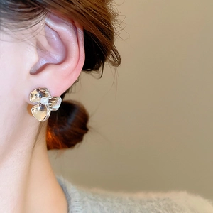 Detail shot of a golden flower earring with a central pearl worn by a model in a side view
