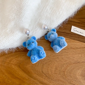 Detail of blue flocked bear earring with silver accents and elegant white pearl stud