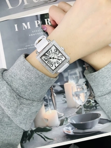 Primer plano de reloj cuadrado con diamantes y correa de cuero blanca en revista