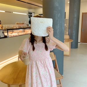 Close-up of a white quilted heart makeup bag held by a woman in a floral dress