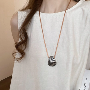 Close-up of a vintage silver shell pendant on a brown braided cord worn by a model