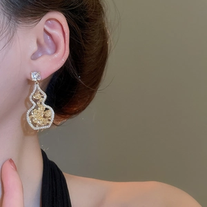 Close-up of gold hollow gourd earrings with rose patterns and sparkling zircon stones