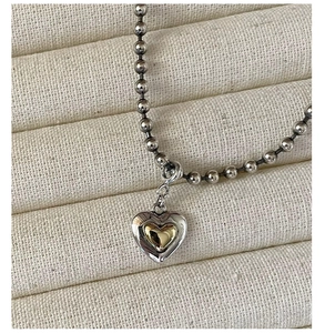 Macro shot of silver and gold heart pendant on a beaded chain over a wavy fabric background