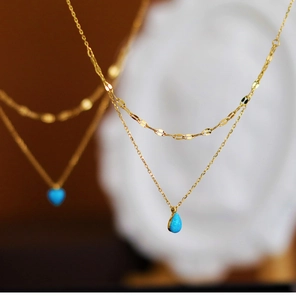 Detail of double-layered gold chain necklace with blue teardrop and heart charms