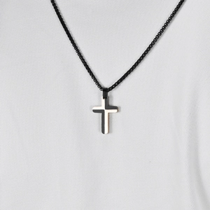 Two-tone stainless steel cross pendant necklace on woven cord with white fabric backdrop