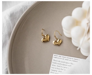 Close-up of polished gold heart-shaped earrings on a minimalist decorative display
