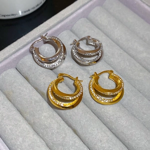 Detail of double-layer intertwined hoop earrings with sparkling zircon inlay in gold and silver