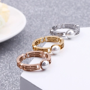 Three-color geometric stainless steel rings with pearl accents on a stone pedestal