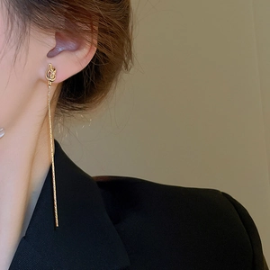 Gros plan de boucles d'oreilles nœuds dorées avec longues chaînes portées par un modèle