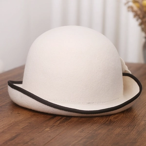 Detail of white wool cloche hat with black wavy scalloped edge on wooden surface