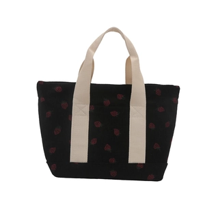 Black corduroy tote bag with red strawberry print and cream handles in a frontal view