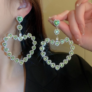 Detailed view of oversized green heart-shaped rhinestone earrings with shimmering star effect