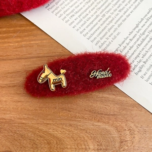 Detail of red plush hair clip with golden pony buckle and handmade metal plate