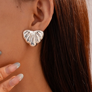 Close-up of silver heart earring with textured shell pattern worn on a female model