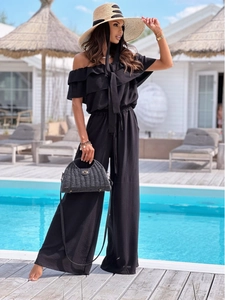 Detail of off-shoulder black jumpsuit with ruffled neckline and textured fabric texture