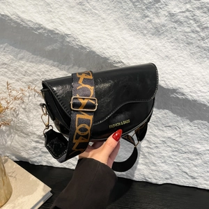 Classic black saddle bag with a patterned wide strap and gold lettering on smooth leather