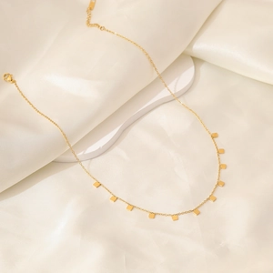 Minimalist gold butterfly necklace with geometric square charms on white silk fabric