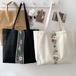 Dettaglio ricamo e bordo in pizzo su una borsa tote minimalista in tela nera e beige