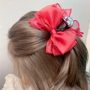 Close-up of a large red organza bow hair claw clip worn by a model in a sweet style
