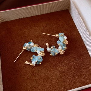 Detailed close-up of C-shaped earrings with light blue stones and pearls on brown velvet