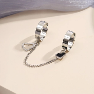 Detail of silver double ring with linked chain and heart pendants on a minimal background