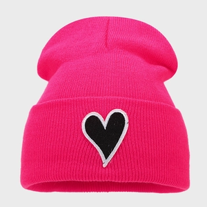Détail du bonnet rose en maille avec écusson brodé en forme de cœur noir
