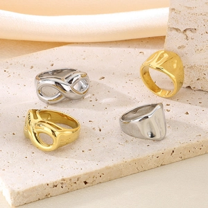 Polished gold and silver sculptural rings on stone background with beige silk fabric