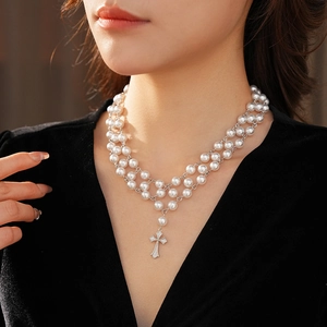 Detail of a three-layer pearl choker with a sparkling silver cross pendant for women