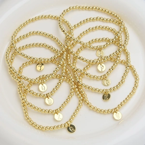 Gold beaded bracelets with round initial letter charms displayed on a ceramic plate