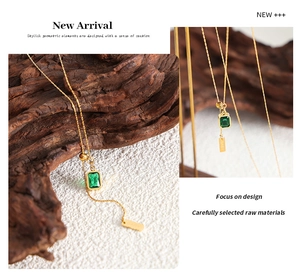 Macro detail of emerald green zircon pendant necklace with gold chain and engraved bar tag