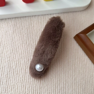 Detail einer braunen Plüsch-Haarklammer mit Perle auf beigem Cord-Hintergrund