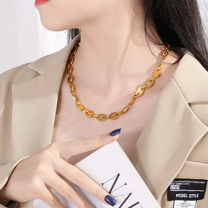 Detail of a gold pig nose chain necklace worn by a model in a beige blazer