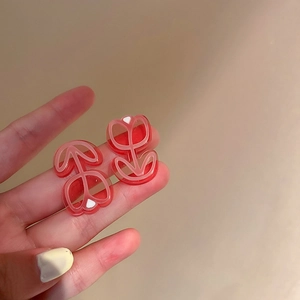 Gros plan de boucles d'oreilles tulipes en résine rouge tenues devant un fond chaud