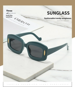Detail of dark green square sunglasses with gold accents on white marble surface