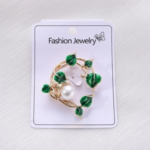 Macro detail of leaf brooch with green enamel, gold finish and central pearl